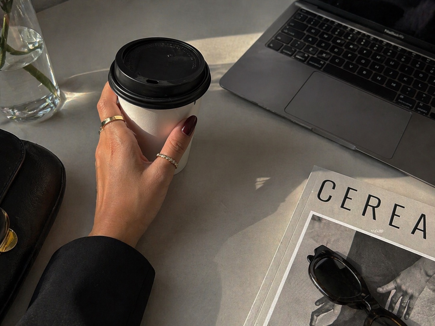Minimal manicure holding coffee beside a laptop and magazine