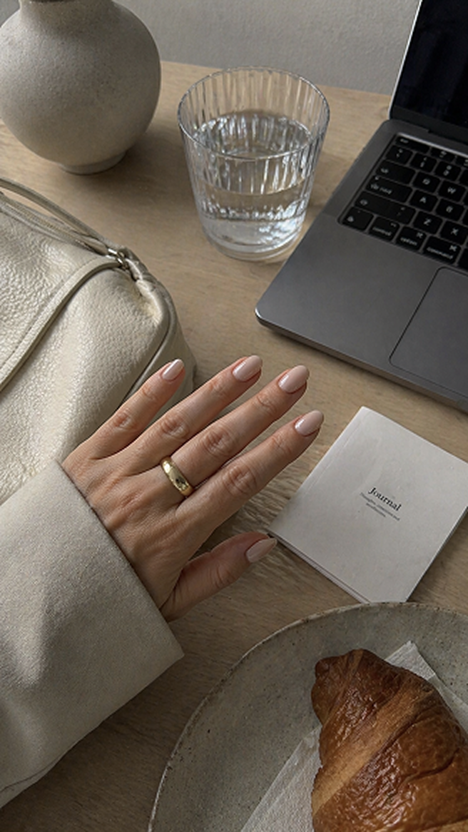 Minimal nude manicure at a cafe table with water and croissant