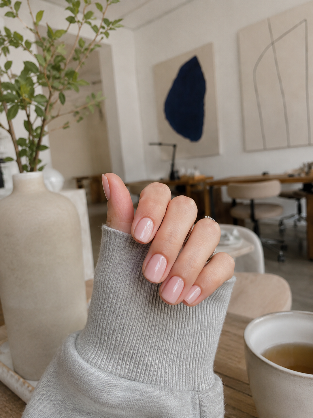 Glossy nude manicure beside a matcha cup and Kinfolk book
