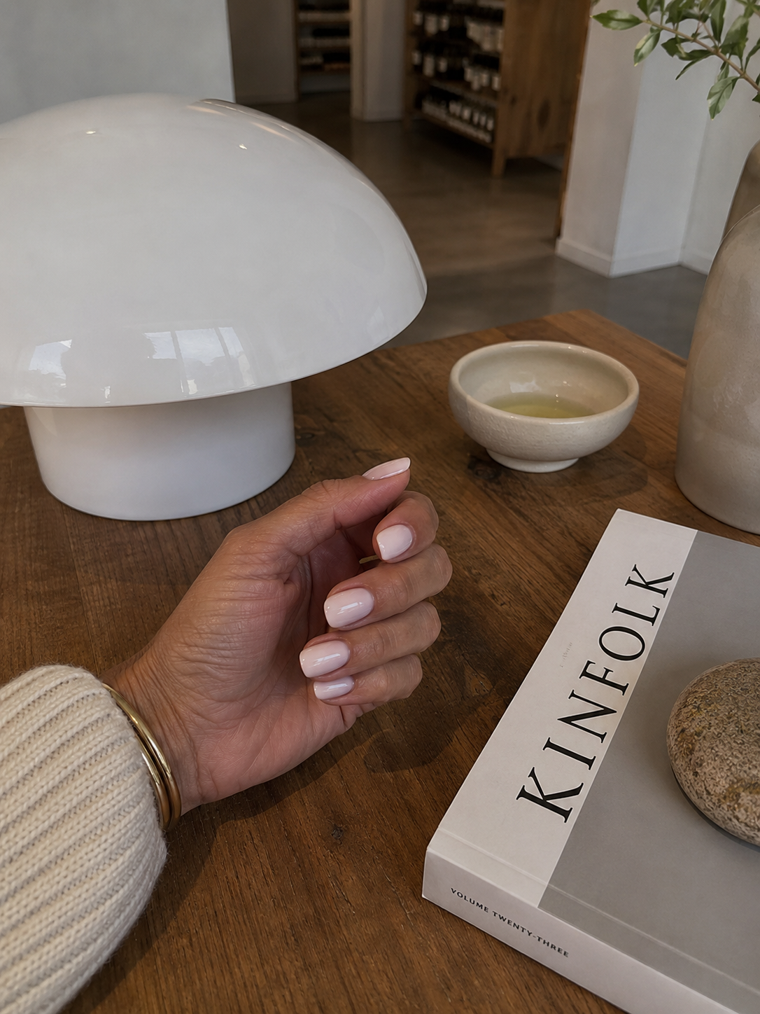 Pale minimalist manicure beside a lamp and Kinfolk book